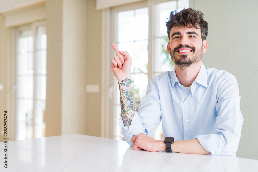 Young businesss man sitting on white table with a big smile on face, pointing with hand and finger to the side looking at the camera. Young businesss man sitting on white table with a big smile on face, pointing with hand and finger to the side looking at the camera.
