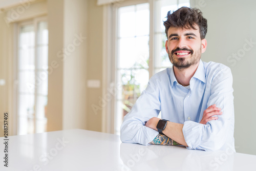 Young businesss man sitting on white table with a happy and cool smile on face. Lucky person.