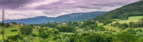 Panorama view of the mountain landscape, trees, forests on the slopes of hills and farmhouses with a cloudy sky in the background,focus plane in the center.Haute-Savoie in France.