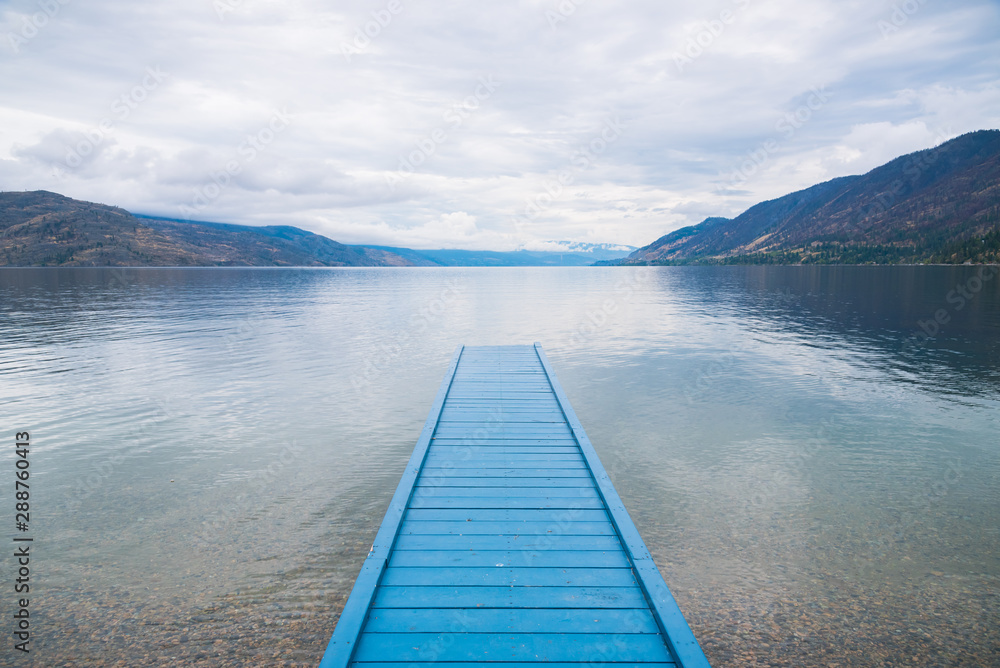 Blue painted dock on lake with view of mountains and cloudy sky