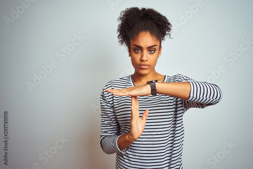 African american woman wearing navy striped t-shirt standing over isolated white background Doing time out gesture with hands, frustrated and serious face
