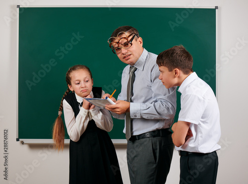 Portrait of a teacher checking homework, reading school exercise books, schoolboy and schoolgirl with old fashioned eyeglasses posing on blackboard background - back to school and education concept photo