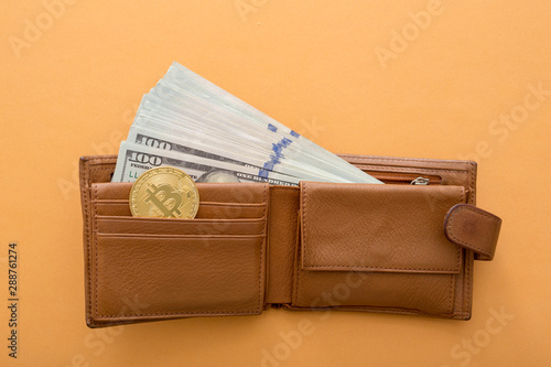 Bitcoin, hundred dollar bills and leather wallet on the orange background. photo