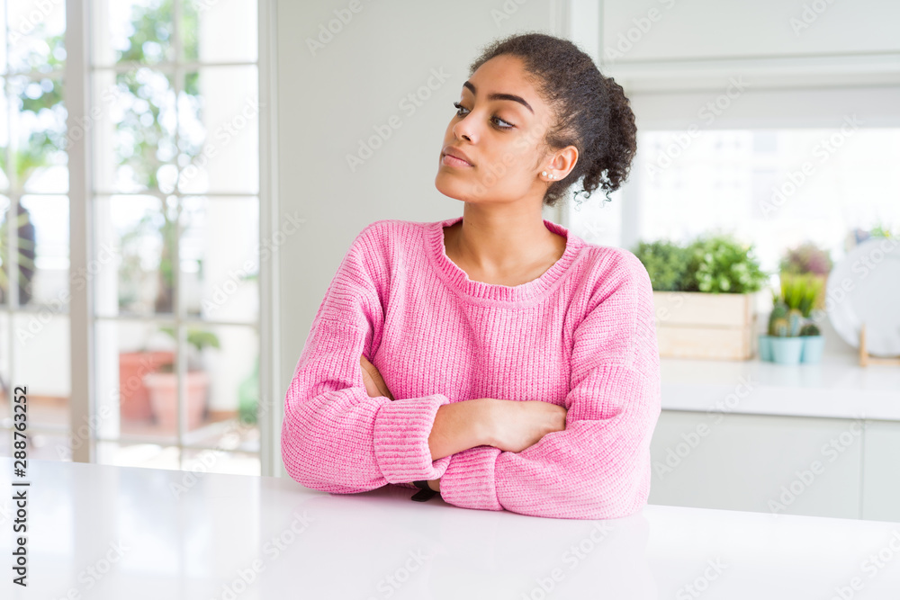 Beautiful african american woman with afro hair wearing casual pink sweater looking to the side with arms crossed convinced and confident Beautiful african american woman with afro hair wearing casual pink sweater looking to the side with arms crossed convinced and confident
