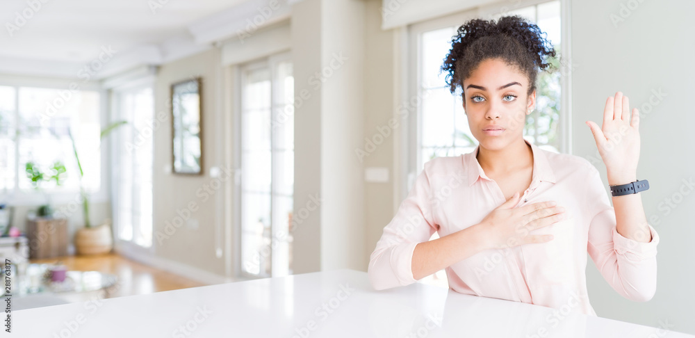 Wide angle of beautiful african american woman with afro hair Swearing with hand on chest and open palm, making a loyalty promise oath Wide angle of beautiful african american woman with afro hair Swearing with hand on chest and open palm, making a loyalty promise oath