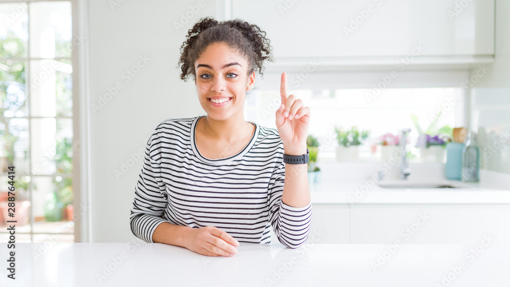 Beautiful african american woman with afro hair wearing casual striped sweater showing and pointing up with finger number one while smiling confident and happy. Beautiful african american woman with afro hair wearing casual striped sweater showing and pointing up with finger number one while smiling confident and happy.
