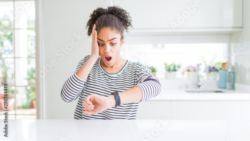 Beautiful african american woman with afro hair wearing casual striped sweater Looking at the watch time worried, afraid of getting late