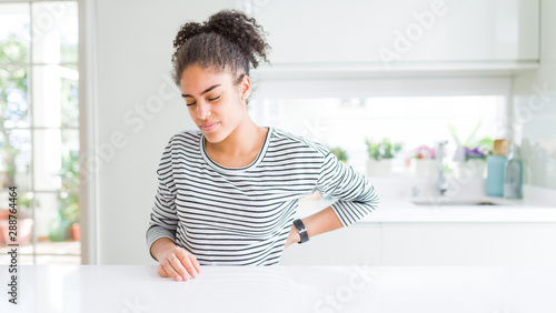 Beautiful african american woman with afro hair wearing casual striped sweater Suffering of backache, touching back with hand, muscular pain