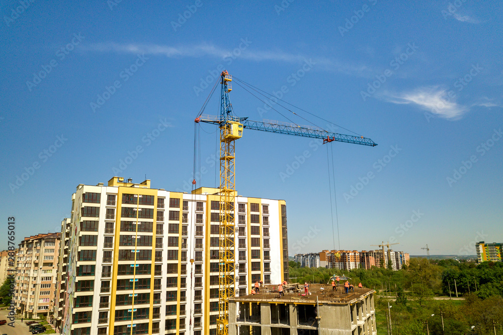 Fototapeta premium Apartment or office tall building under construction. Working builders and tower cranes on bright blue sky copy space background.