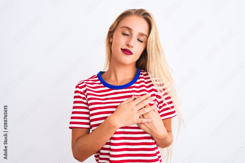 Young beautiful woman wearing red striped t-shirt standing over isolated white background smiling with hands on chest with closed eyes and grateful gesture on face. Health concept. Young beautiful woman wearing red striped t-shirt standing over isolated white background smiling with hands on chest with closed eyes and grateful gesture on face. Health concept.