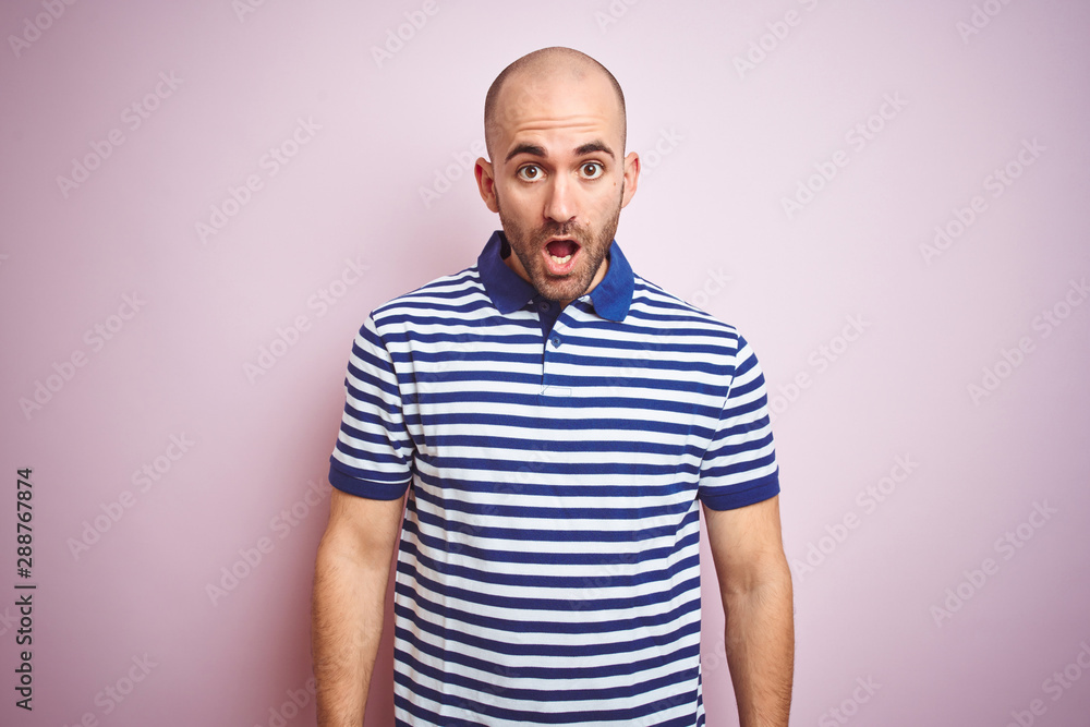 Young bald man with beard wearing casual striped blue t-shirt over pink isolated background afraid and shocked with surprise expression, fear and excited face. Young bald man with beard wearing casual striped blue t-shirt over pink isolated background afraid and shocked with surprise expression, fear and excited face.