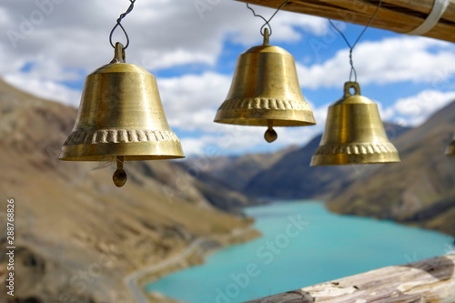 CLOSE UP: Three golden bells hang on top of hill overlooking Manak Dam Lake.