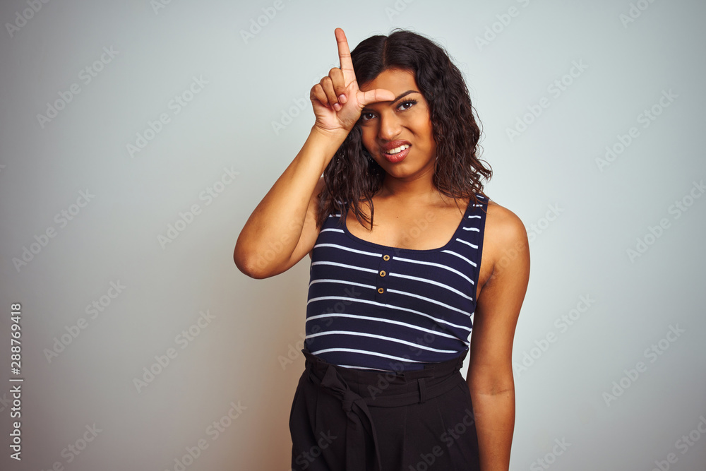 Transsexual transgender woman wearing striped t-shirt over isolated white background making fun of people with fingers on forehead doing loser gesture mocking and insulting. Transsexual transgender woman wearing striped t-shirt over isolated white background making fun of people with fingers on forehead doing loser gesture mocking and insulting.