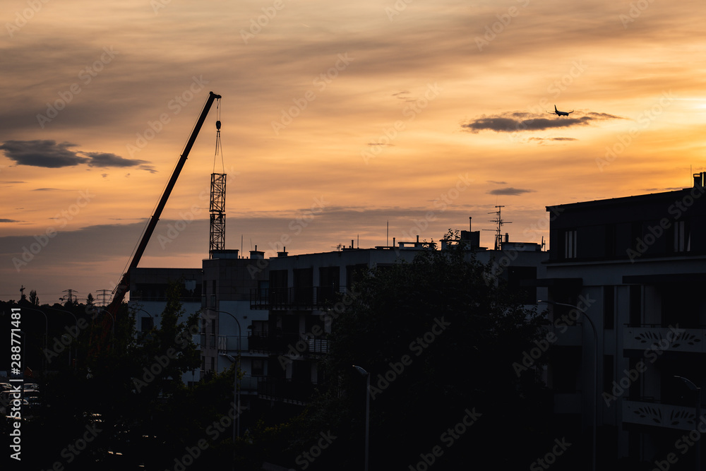 Installation of the crane over silhouette of buildings with airplane and sunset in the background.