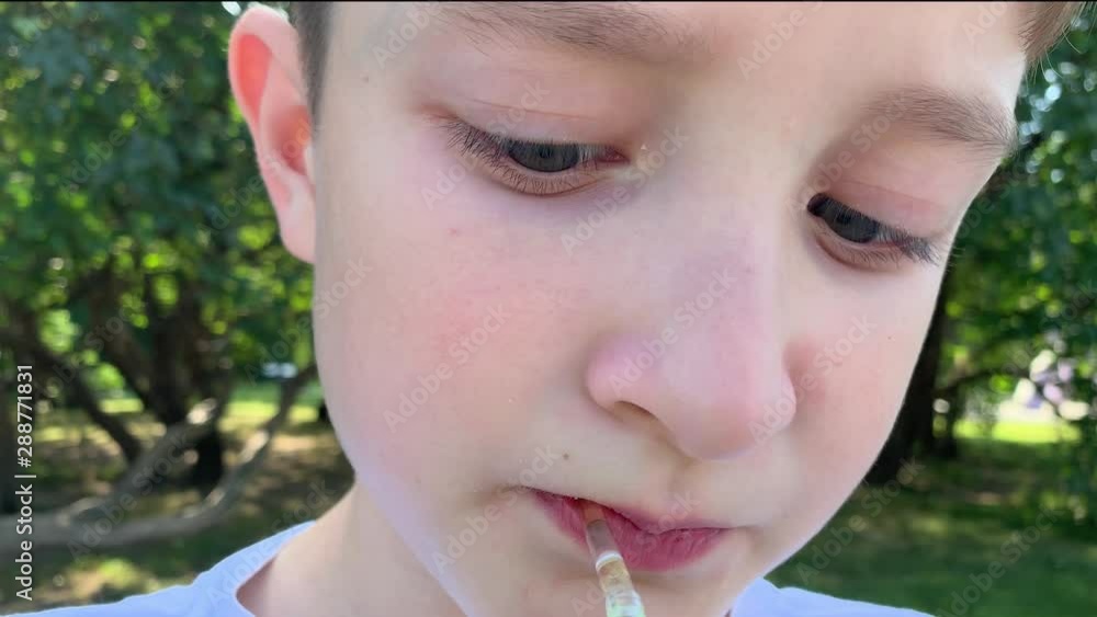 A young preteen caucasian boy sitting in summer city park and drinking juice through a straw from the paper juice pack, close up view, takeaway fastfood concept A young preteen caucasian boy sitting in summer city park and drinking juice through a straw from the paper juice pack, close up view, takeaway fastfood concept