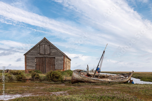 Days Gone By / An image of an old coal barn and fishing boat on a waterway illustrating days gone by at Thornham Norfolk, England, UK. photo