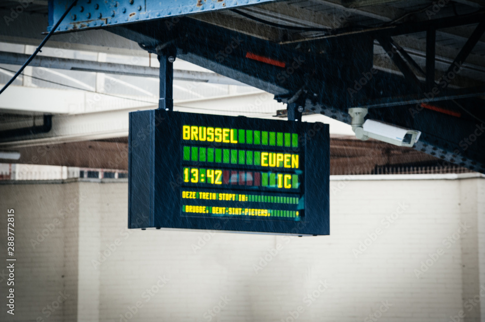 Fototapeta premium Rain water drops in front of defocused arrival departure board in Belgium Ostend train station with destination Brussels Eupen