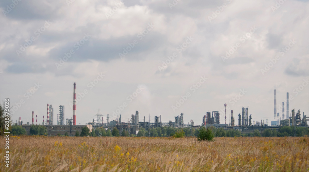 panoramic  view of the refinery with high striped pipes and yellow autumn field
