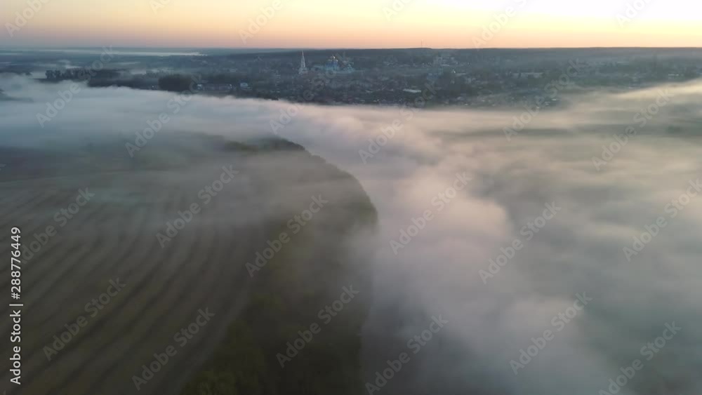 Flying through the clouds above river with small town on background at Wonderful morning sunrise. Natural Landscape Flying through the clouds above river with small town on background at Wonderful morning sunrise. Natural Landscape