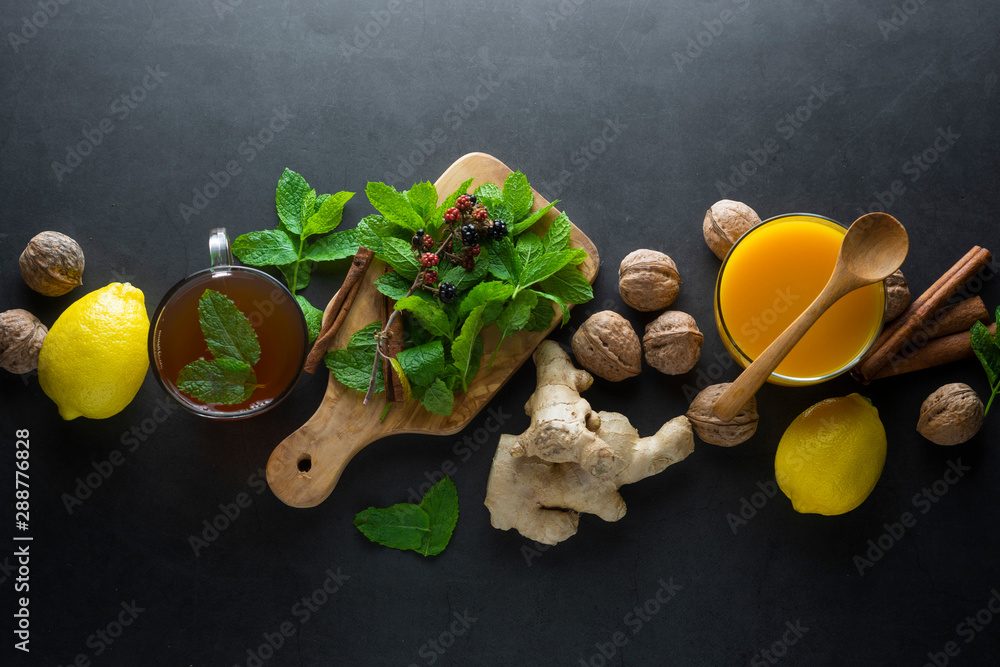 Ginger tea cup with lemons and mint leaves on dark background. Ginger tea, drink ingredients, cold and autumn time. Ginger tea cup with lemons and mint leaves on dark background. Ginger tea, drink ingredients, cold and autumn time.