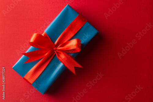 Blue gift box with red ribbon and bow isolated on red background, top view. Christms, party concept.
