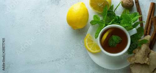 Glass cup of ginger tea with lemons and mint leaves on light background. Ginger tea, drink, cold and autumn time. Banner.