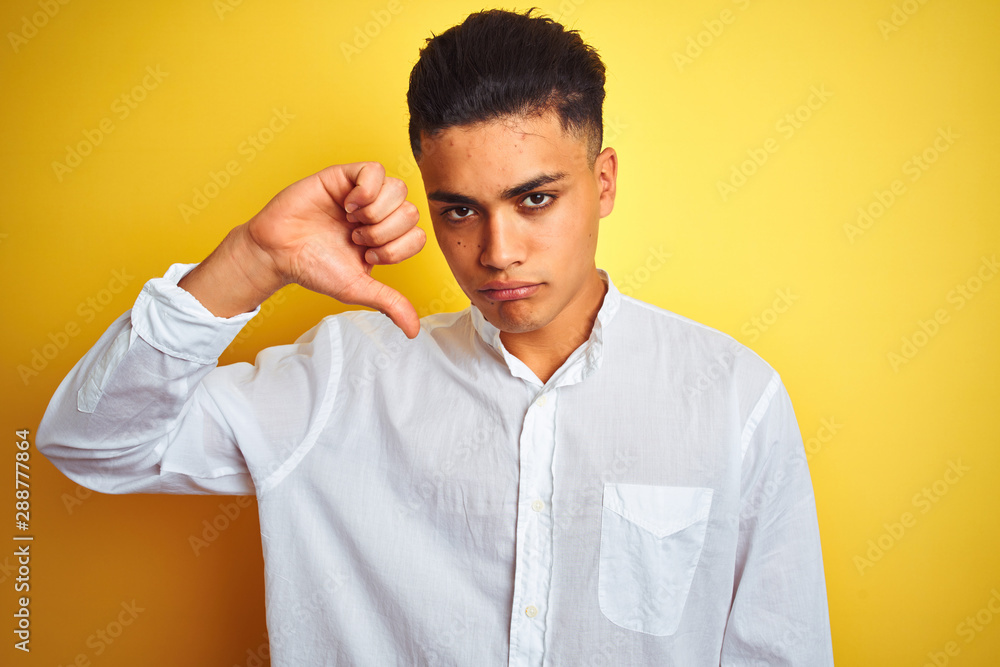 Young brazilian businessman wearing elegant shirt standing over isolated yellow background with angry face, negative sign showing dislike with thumbs down, rejection concept Young brazilian businessman wearing elegant shirt standing over isolated yellow background with angry face, negative sign showing dislike with thumbs down, rejection concept