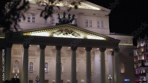 Beautiful facade of the Bolshoi Theater, Moscow. Building was built in 1776. Night time, Main entrance, which is decorated with stucco molding and stunning statues. In the foreground are tree branches