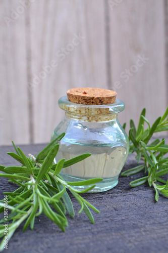 Essential oil with rosemary plant on wooden background, vertical photo