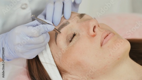 Canvas Print Closeup part of face, woman plucking eyebrows depilating with tweezers