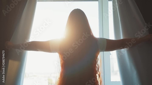 Slow motion with young woman opens dark curtains in morning and looks at morning sun light photo