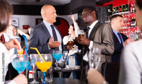 Two cheerful male colleagues enjoying corporate bar party, drinking beer and having fun conversation