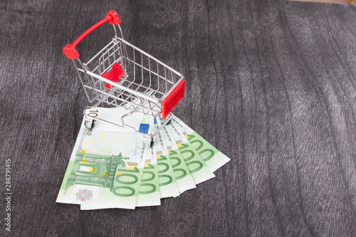 Shopping Cart Full of Cash. Shopping consept, euro money in cart. Shopping cart with euro banknotes on grey desk. Copy space for text.