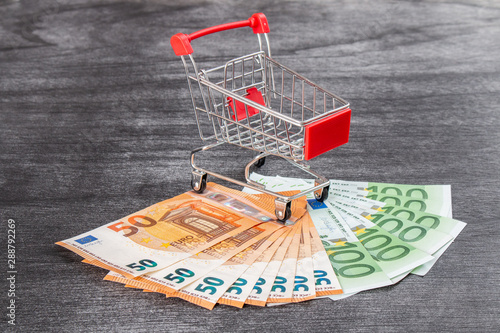 Shopping Cart Full of Cash. Shopping consept, euro money in cart. Shopping cart with euro banknotes on grey desk. Copy space for text.