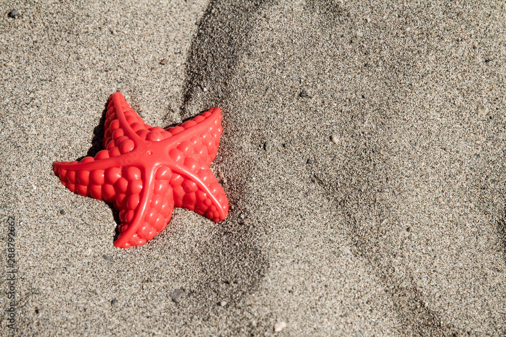 Childs starfish plastic beach toy in the sand; making impressions in the sand on a beach Childs starfish plastic beach toy in the sand; making impressions in the sand on a beach