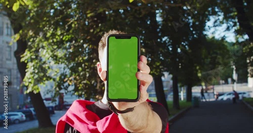 Young man showing in hand mock-up chromakey greenscreen with modern application copy space outdoor in sunny weather. photo