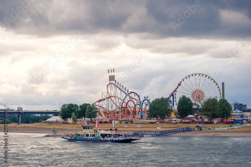 Outdoor scenery view of Rheinkirmes, Annual amusement park festival, on riverside of Rhine river during sunset time and background of cloudy and stormy sky in Düsseldorf, Germany.