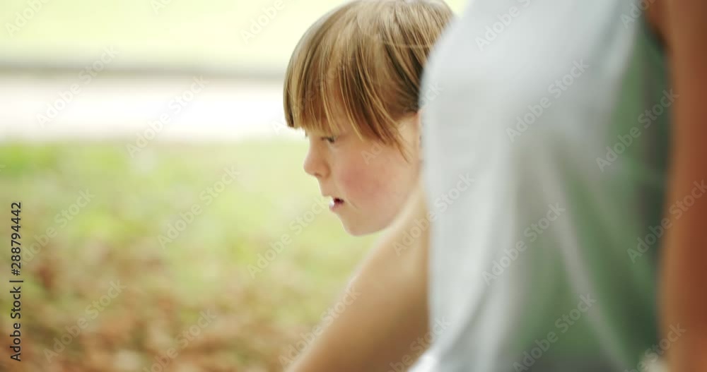 Little Down syndrome boy walking with mother in park and chatting, spending time together Little Down syndrome boy walking with mother in park and chatting, spending time together