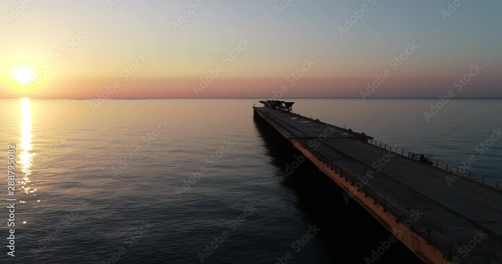 vuelo dron sobre final puente pantalan de puerto abandonado en un amanecer anaranjado y el sol despuntando