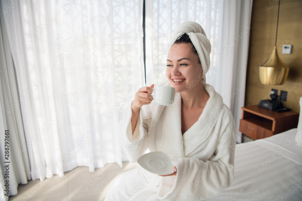 A girl in a bathrobe drinking coffee in the morning on the windowsill. A girl in a bathrobe drinking coffee in the morning on the windowsill.
