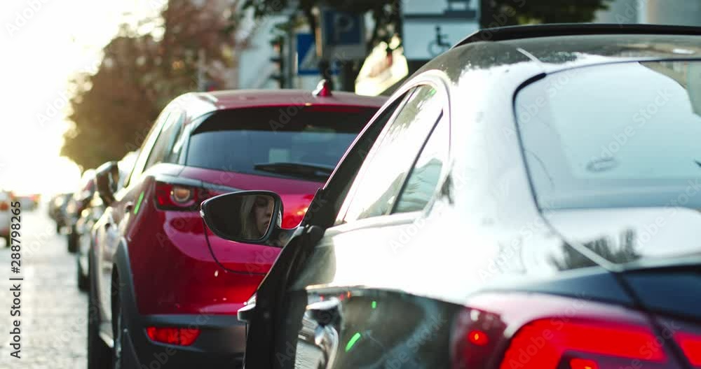 Glamorous young blonde woman in film look parking car on busy road wearing sunglasses staying in the city center. Glamorous young blonde woman in film look parking car on busy road wearing sunglasses staying in the city center.