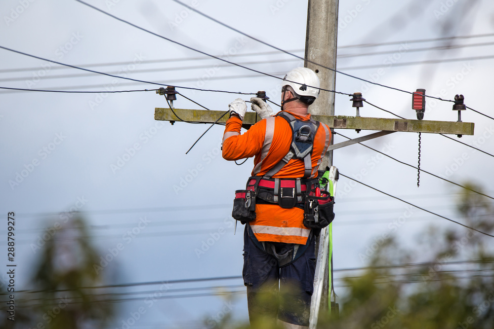 A linesman with a power company connects a new house in a rural area to the main network - obrazy, fototapety, plakaty 