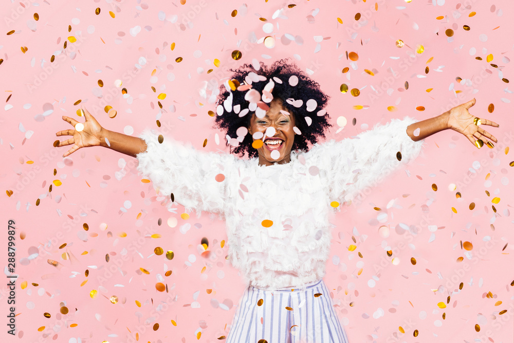 Happy young woman celebrating with arms out and lots of falling confetti - obrazy, fototapety, plakaty 