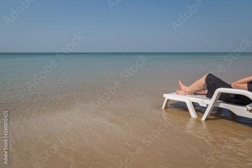 Vacation on tropical beach Woman's legs on the beach bed with clear ocean water