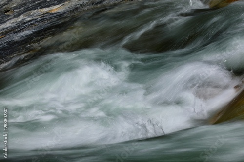 smooth looking white and dark water, rendered with a slow shutter speed, flows quickly in a Sierra Nevada mountain stream in California 