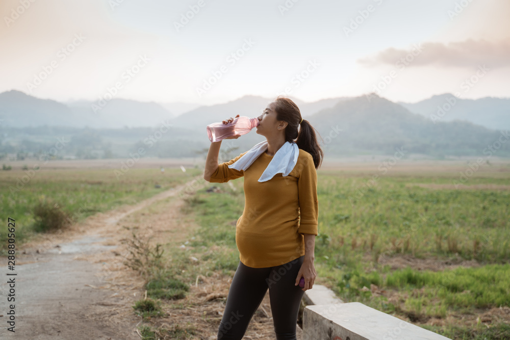 thirsty pregnant woman after workout drinking a bottle of water