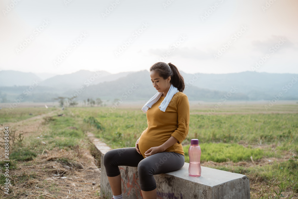 pregnant woman sit while jogging outdoor take a break