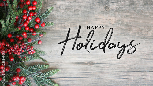 Happy Holidays Text with Holiday Evergreen Branches and Berries Over Rustic Wooden Background photo