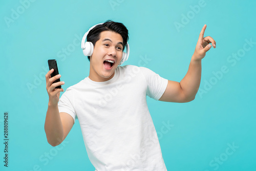 Happy young Asian man wearing headphones moving body while listening to music