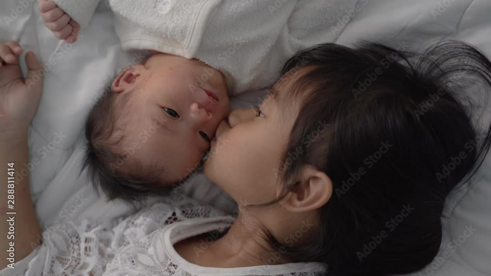 asian daughter kid with infant sibling playing on bed wearing white together asian daughter kid with infant sibling playing on bed wearing white together